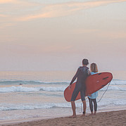 Surferpärchen im Abendlicht bei kleinen grünen Wellen am Hausstrand in Jandía